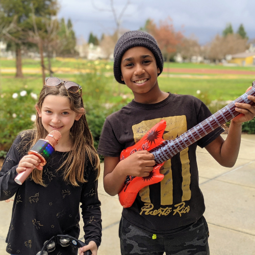 A girl with a mic and boy with a plastic electric guitar in park